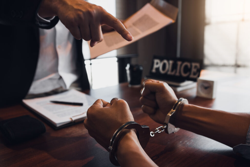 The police officer pointed the handcuffs and held the documents to arrest the accused in a fraud case.
